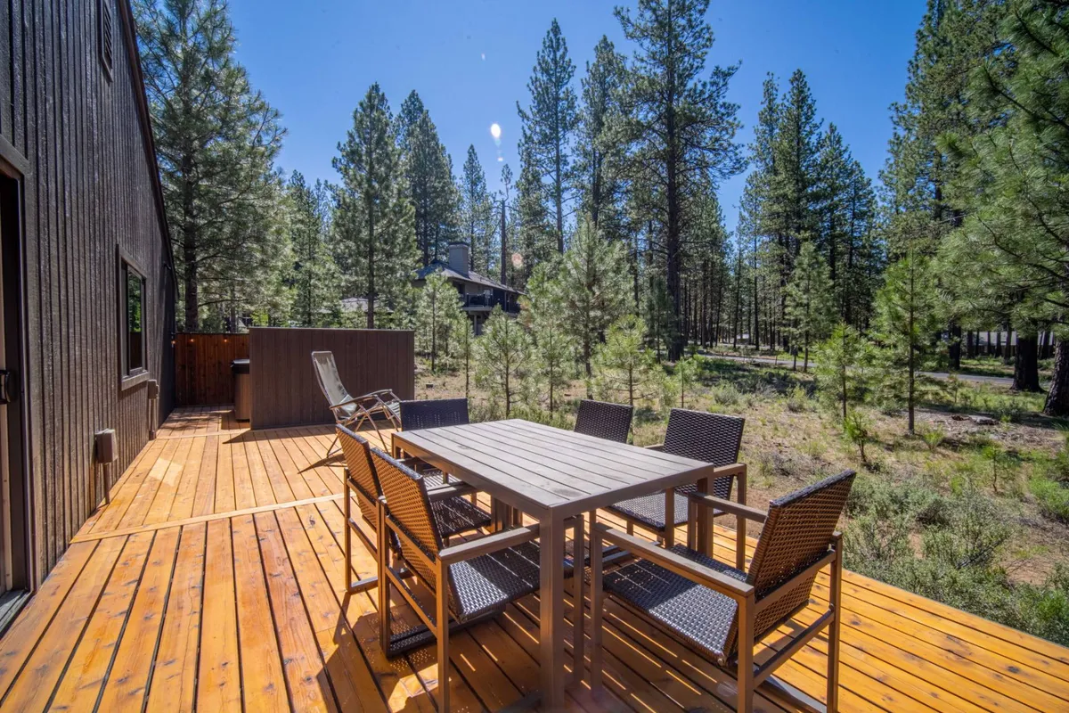 The image showcases a spacious wooden deck nestled among tall pine trees, featuring a large dining table with outdoor chairs set for a group gathering. The tranquil setting is ideal for al fresco meals, relaxing in nature, and enjoying the serene beauty of Sunriver. The deck invites guests to unwind, dine together, and experience the peaceful ambiance of the surrounding forest.