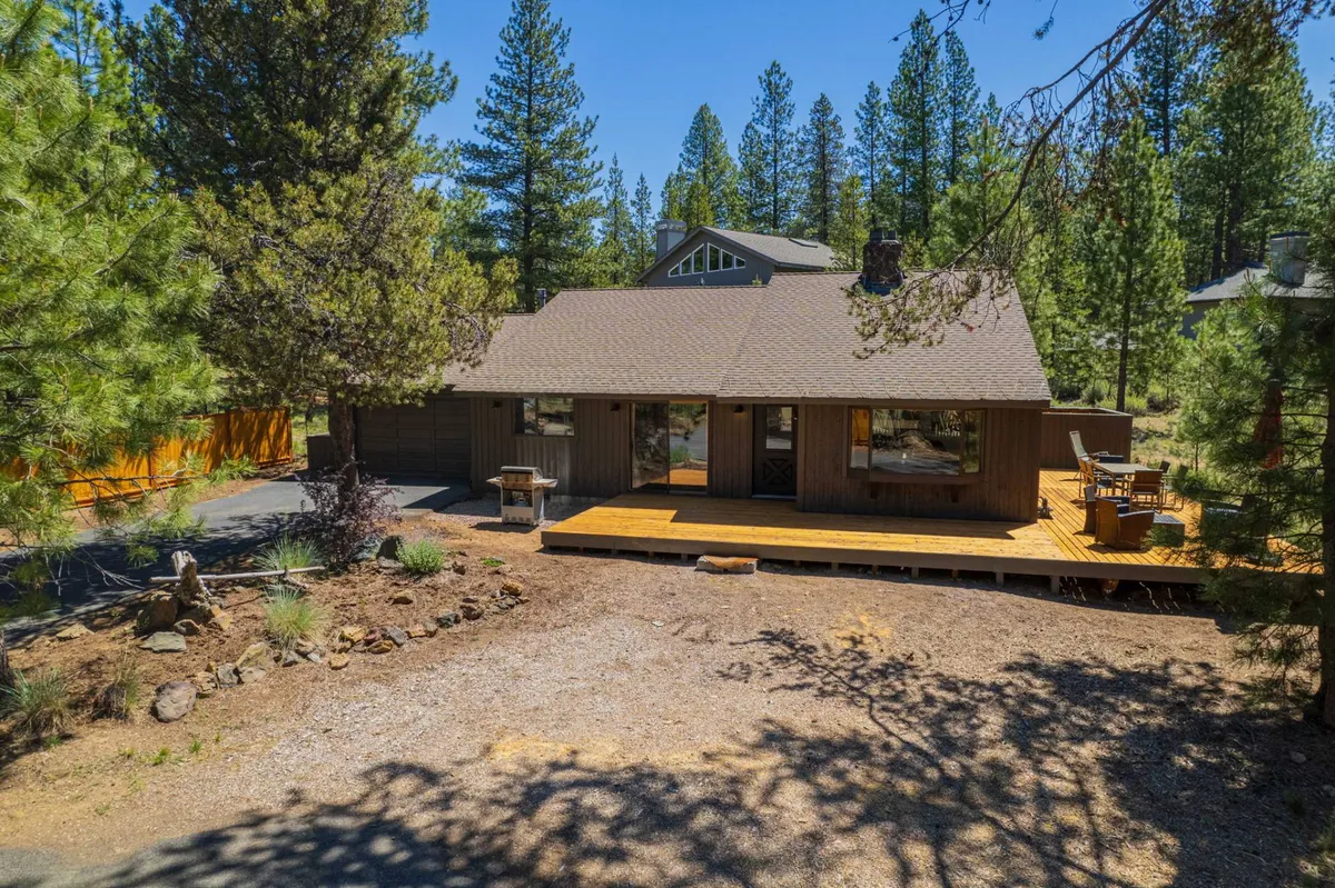 A tranquil deck area with outdoor seating, large windows facing surrounding pine trees, and ample space for family gatherings or stargazing. The atmosphere is relaxing and welcoming, ideal for group meals and unwinding after a day of adventure.
