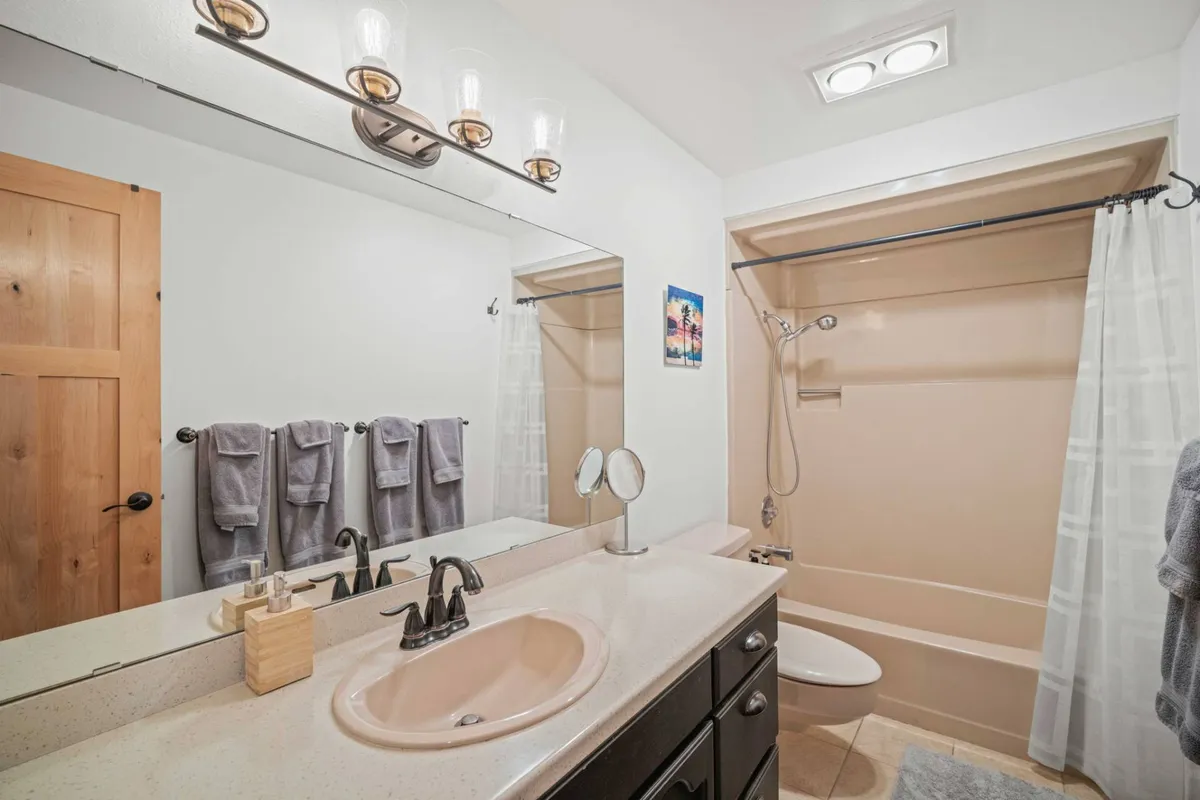 A modern, welcoming bathroom featuring a mirror, sink, shower area, fluffy towels, and a well-placed light fixture. The space is clean and functional, inviting guests to relax and refresh.