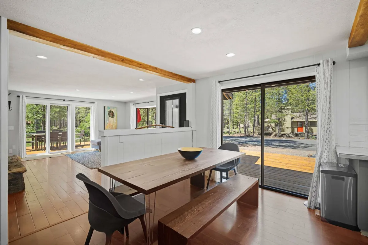 A welcoming dining area with a sturdy wooden table, sliding glass doors that offer a view to the deck, and exposed wooden beams overhead. The scene is set for family meals, with sunlight spilling in to create a cozy, communal atmosphere.
