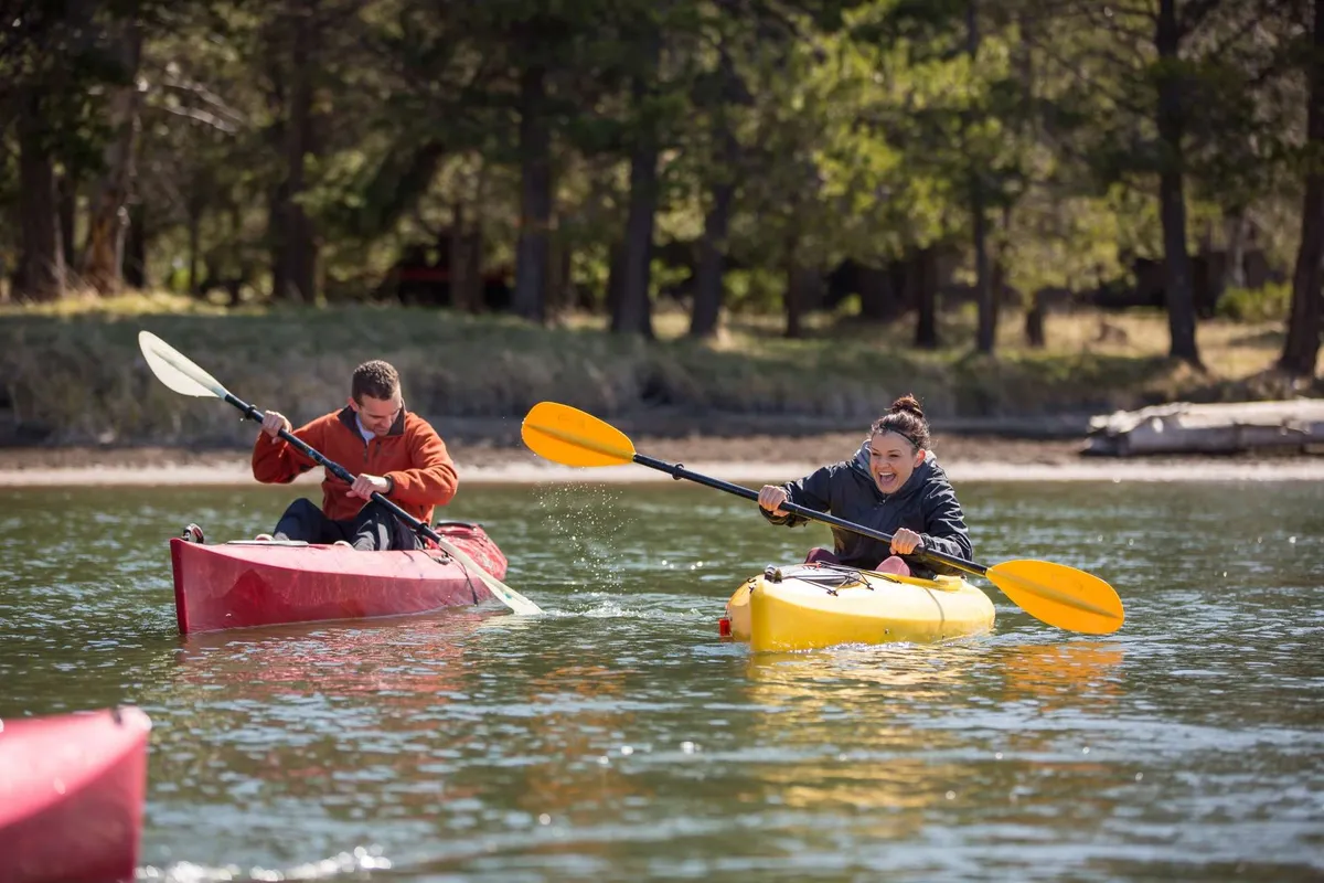 Two kayakers paddle along calm water bordered by lush greenery, embodying outdoor adventure and a sense of active fun. The bright scene radiates summer energy and highlights opportunities for river activities close to the property.