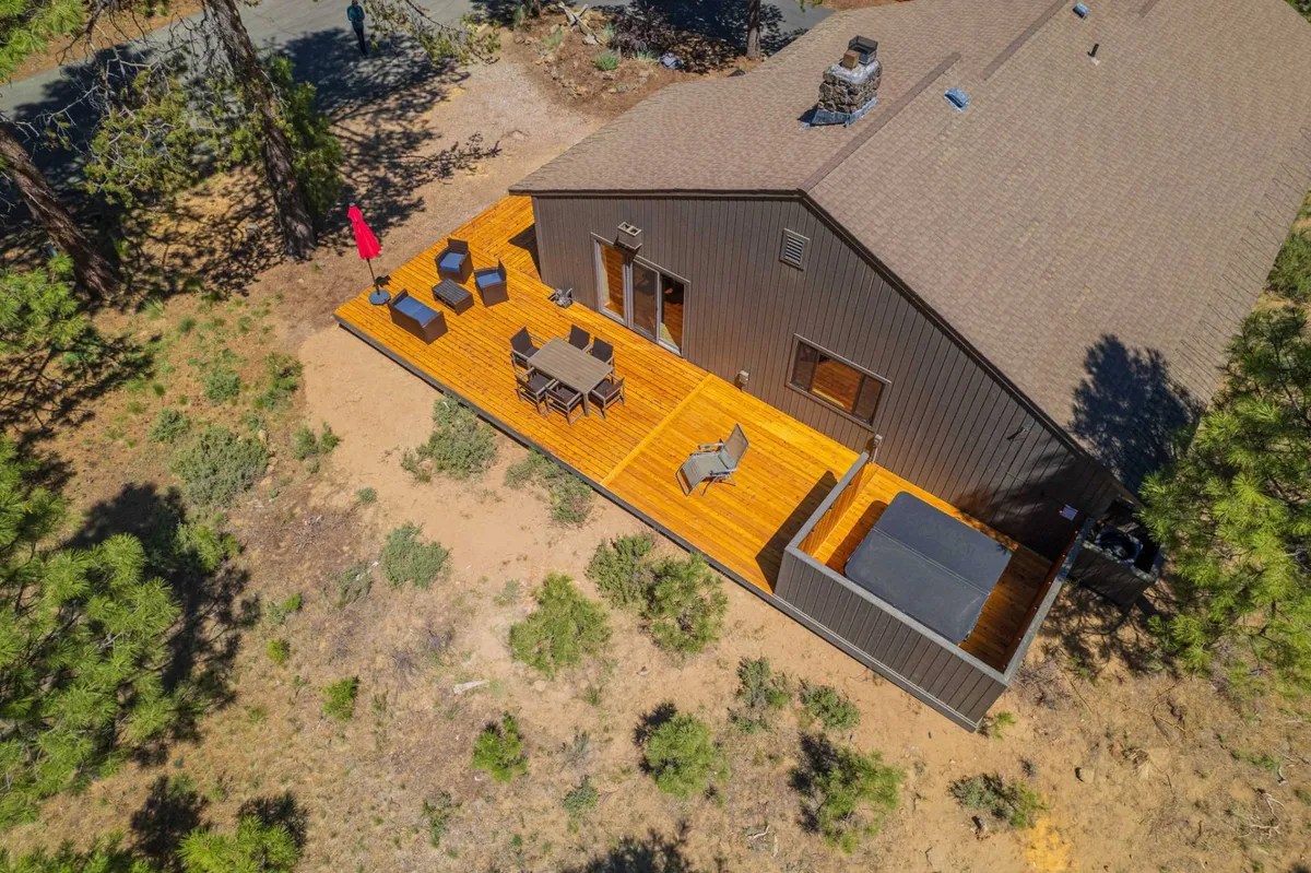 This image showcases a spacious wooden deck with a private hot tub, outdoor seating area, and a red umbrella, all nestled among tall pine trees. The area appears tranquil and inviting, with the hot tub and seating capturing the essence of outdoor relaxation and social gatherings.
