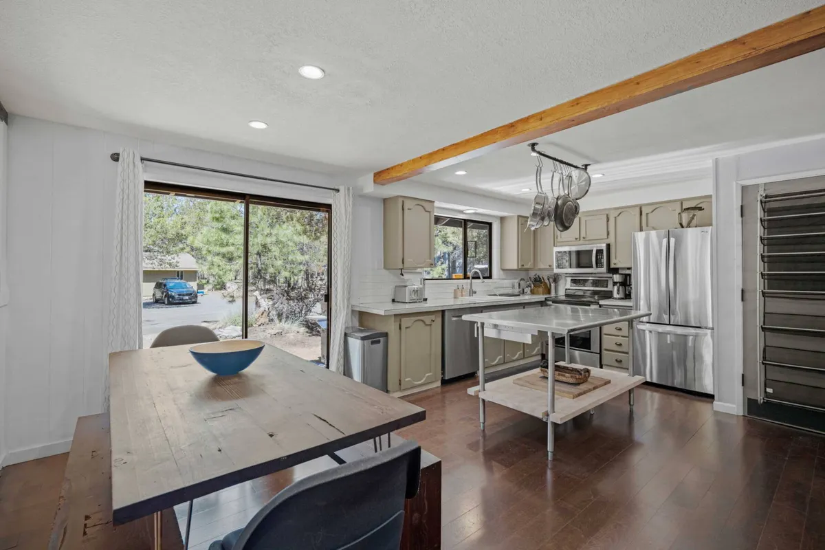 This image features an inviting interior space with both a kitchen island and a rustic-chic dining table set against a large window, allowing ample natural light to fill the room. The kitchen is equipped for group cooking, while the dining area is perfect for sharing meals and conversations.