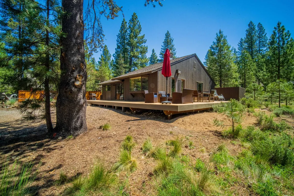 A peaceful wooden deck with a red umbrella and outdoor seating, enveloped by tall trees. The setup evokes a sense of relaxation and immersion in the natural environment—ideal for evening stargazing, morning coffee, or sunset dinners.
