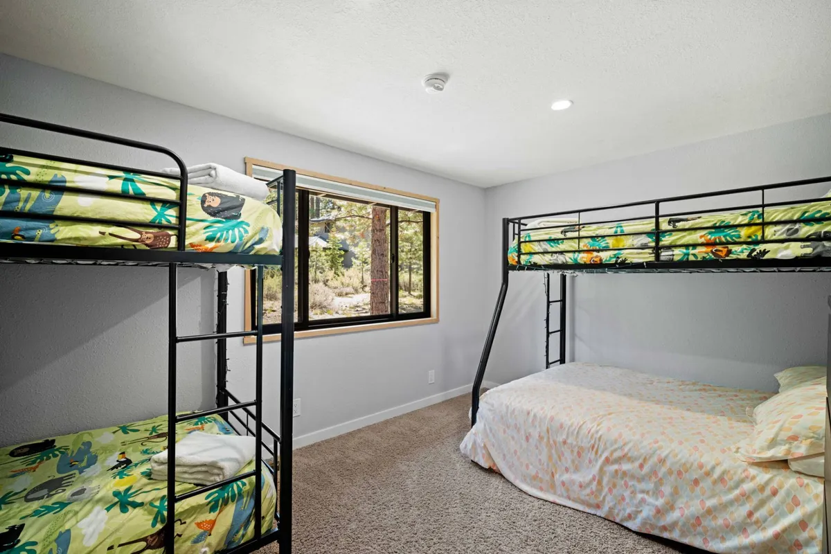 A playful bunk room with sturdy bunk beds, plush bedding, and a window providing natural light. The space feels fun and welcoming, ideal for children or those young at heart.